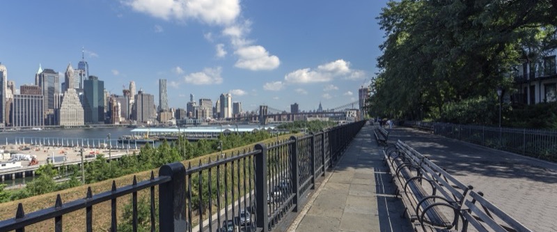 Stone-paved Brooklyn Heights Promenade with benches, trees and the Lower Manhattan skyline across the East River